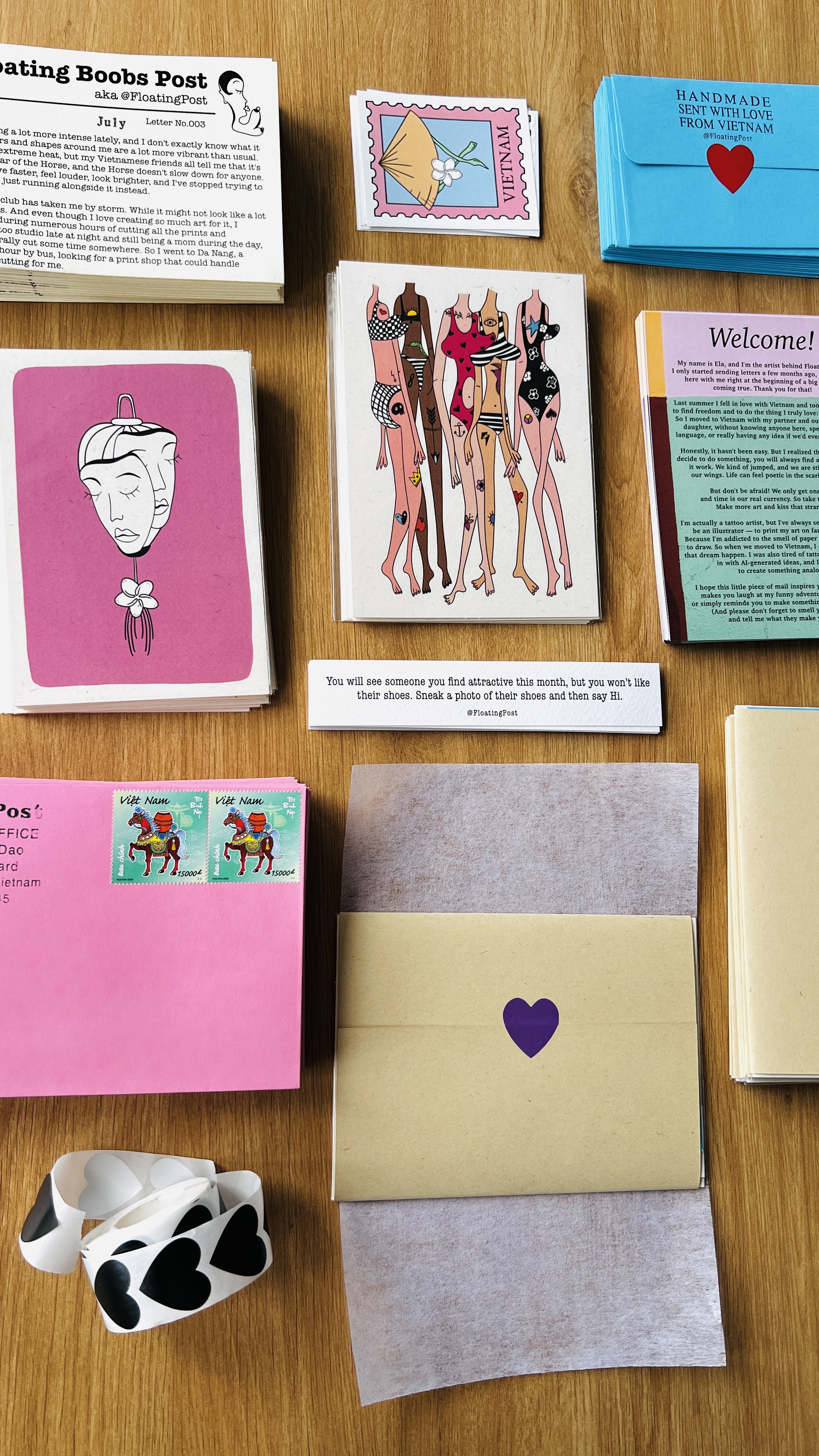 A flatlay of the July letter, fortune strip, art prints and welcome letter beside pink, tan and blue Floating Post envelopes